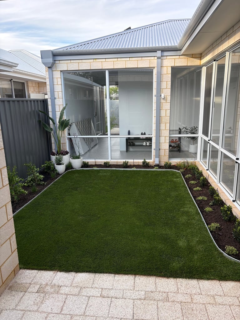 Modern backyard with artificial turf, paved patio, and brick home with glass enclosed porch area