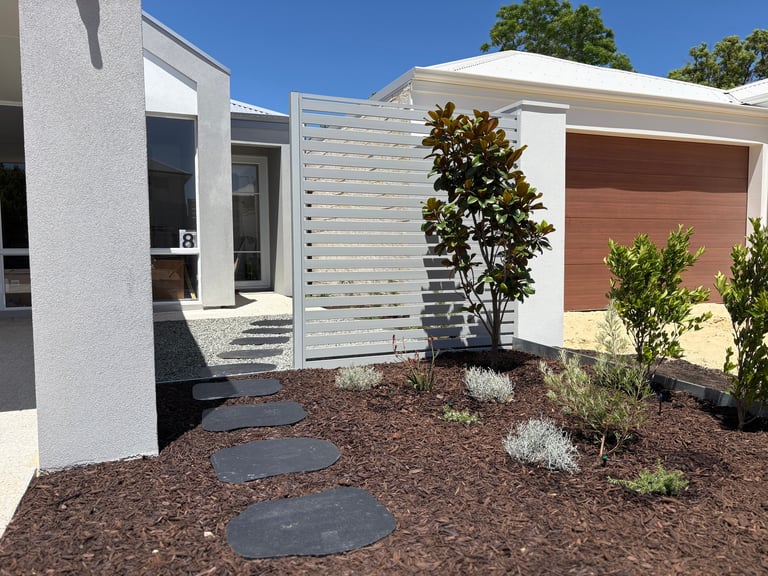 Modern white house with horizontal slatted fence, mulch landscaping, stepping stones, and metal garage door