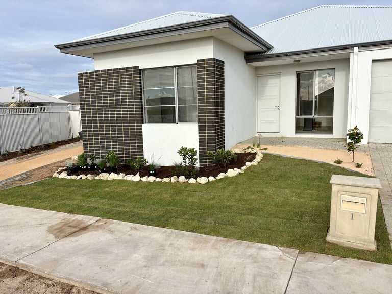 Modern single-story white house with dark green tile accent wall, manicured lawn, concrete driveway, and mailbox in front yard