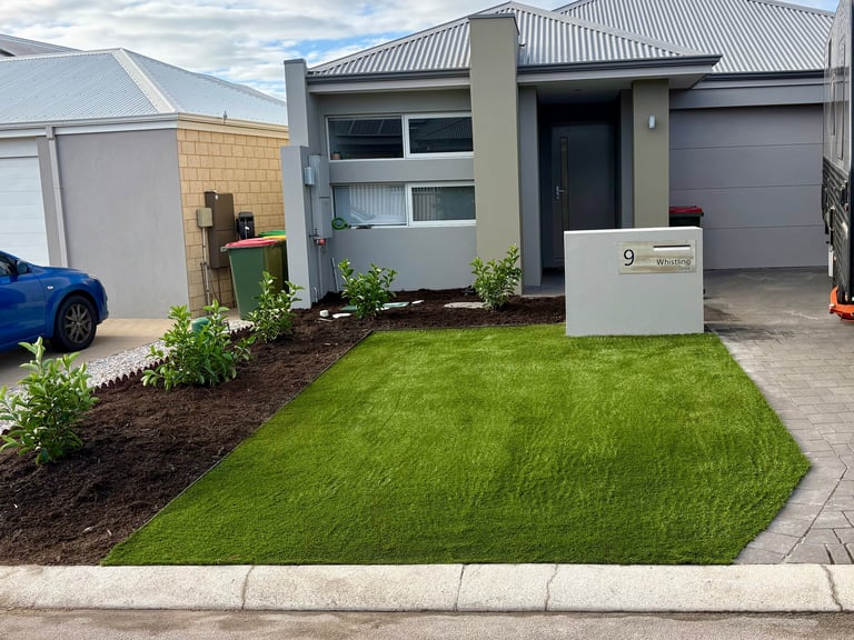 Modern single-story home with manicured green lawn, landscaping, white letterbox, and paved driveway with parked blue car