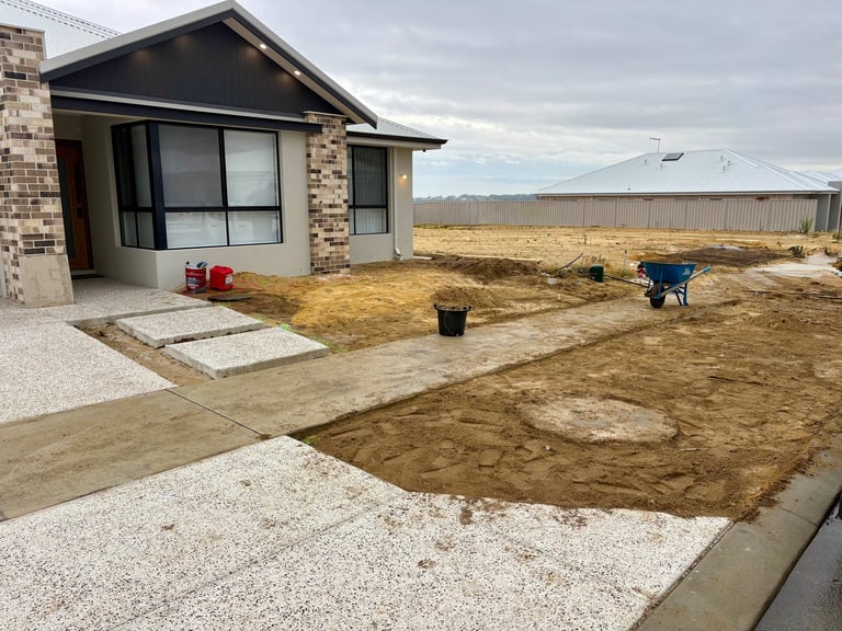 New brick home with bare dirt yard under construction, showing gravel pathways and landscaping materials