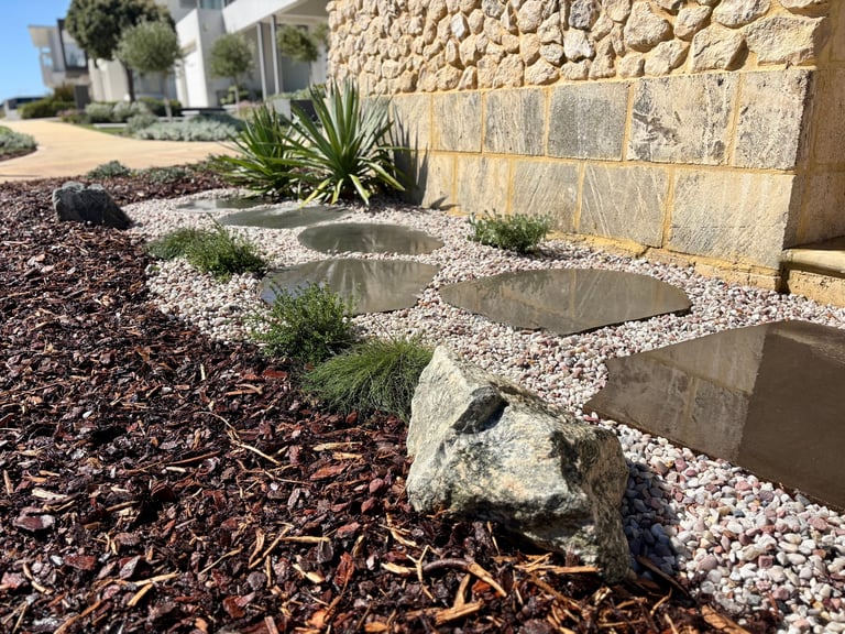 Desert landscaping with mulch, gravel, succulents, and stone features against a stucco wall